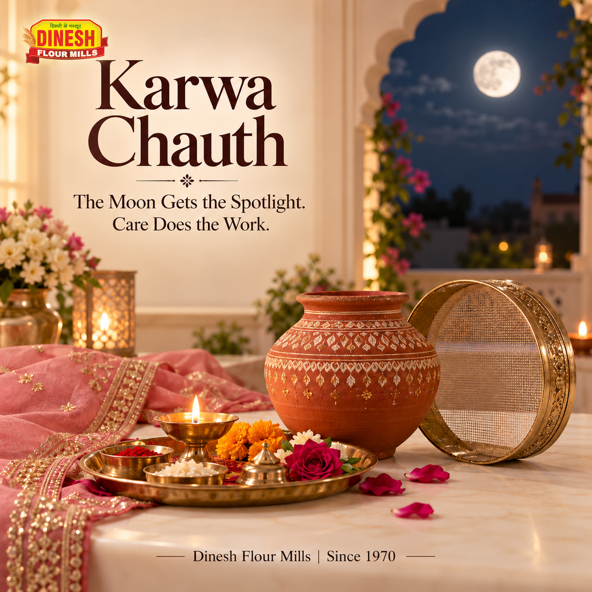 n earthen karva, sieve and flower-filled puja thali on a cream table with the moon visible through an arch.
